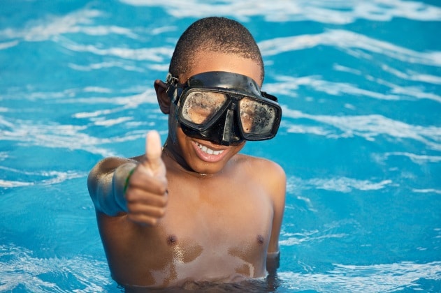 little boy wearing goggles in pool giving thumbs up