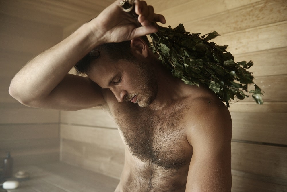A man with a broom in his hand is relaxing in the sauna